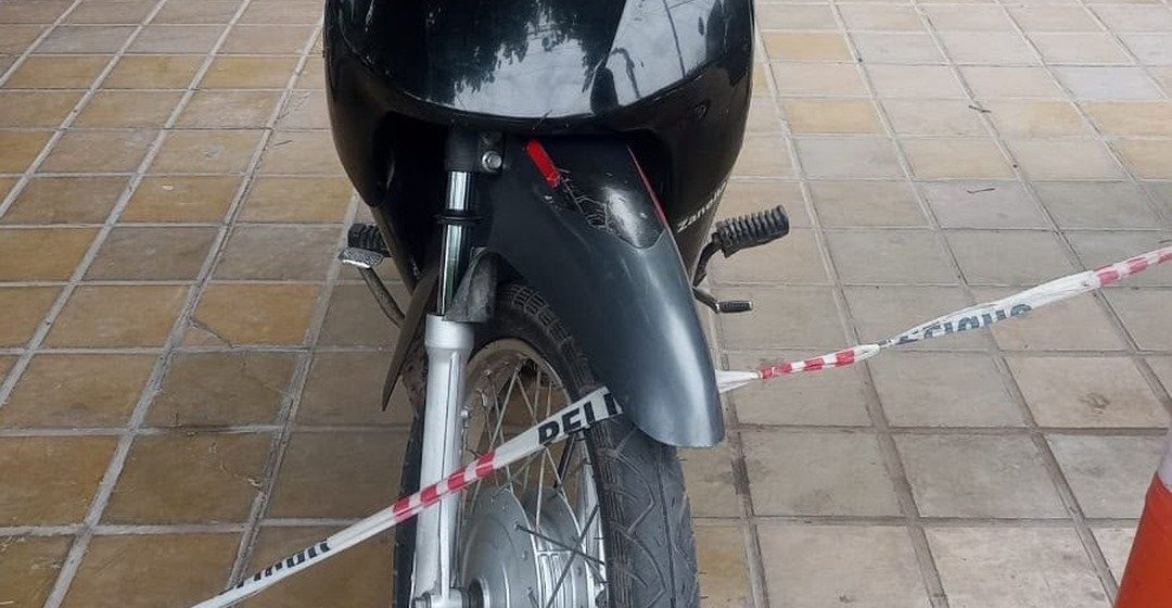 Una moto negra detrás de una cinta policial, sobre una vereda.