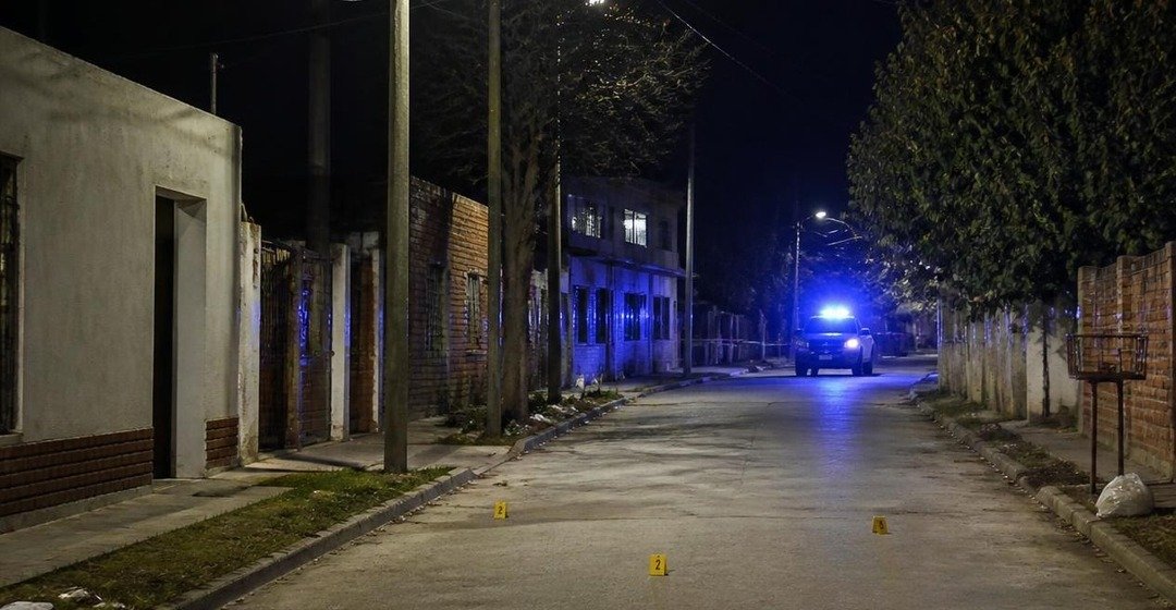 Calle de barrio de noche con un patrullero a lo lejos. Imagen ilustrativa.