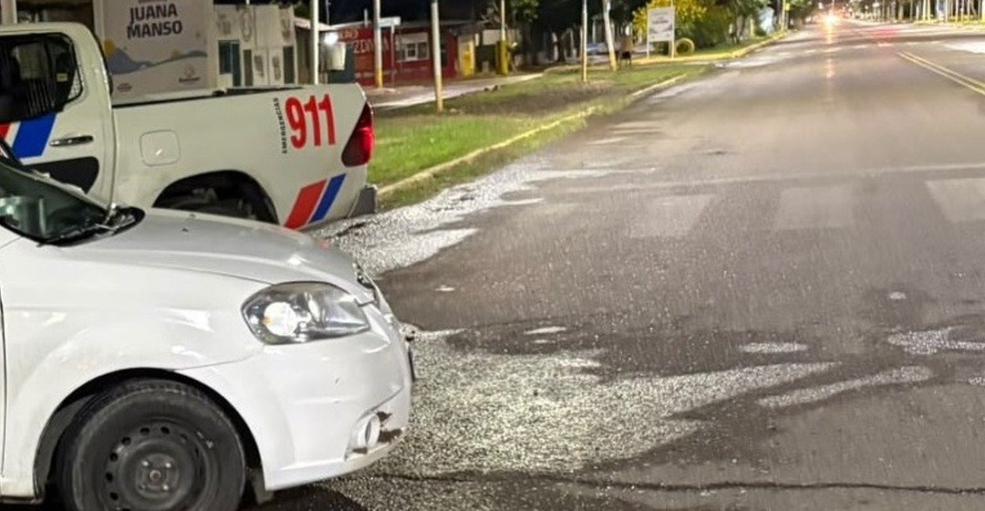 Un Chevrolet Aveo blanco junto a una camioneta policial 911 en una calle de Rawson.