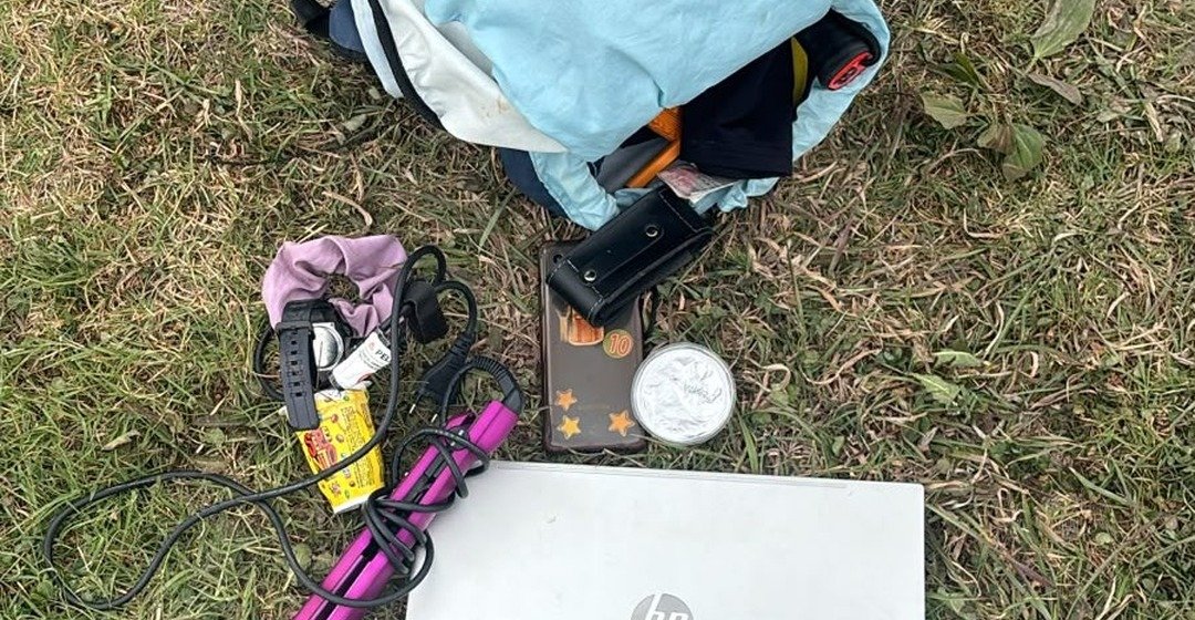 Mochila, notebook y otros objetos recuperados por la Policía sobre el pasto.