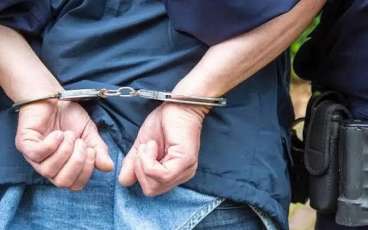 Persona esposada con las manos en la espalda junto a un policía. Imagen ilustrativa.