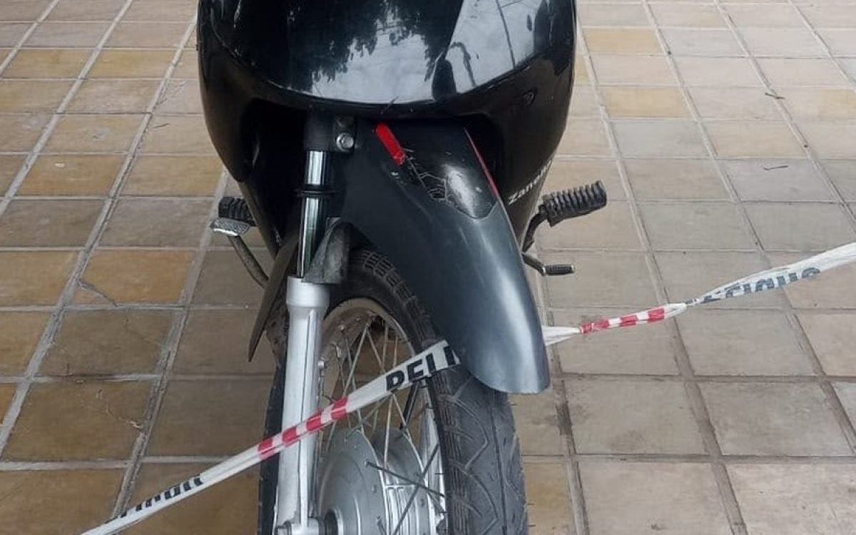 Una moto negra detrás de una cinta policial, sobre una vereda.
