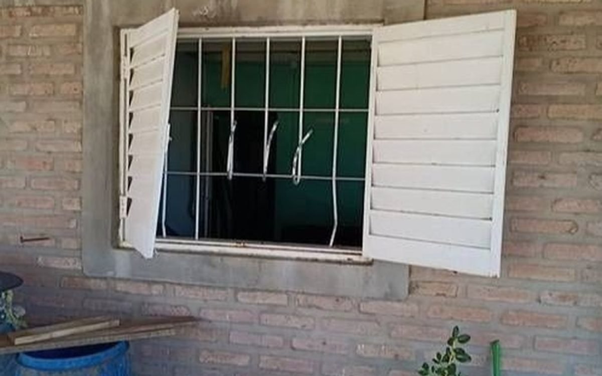 Ventana de una vivienda de ladrillo con las persianas abiertas y las rejas dobladas.
