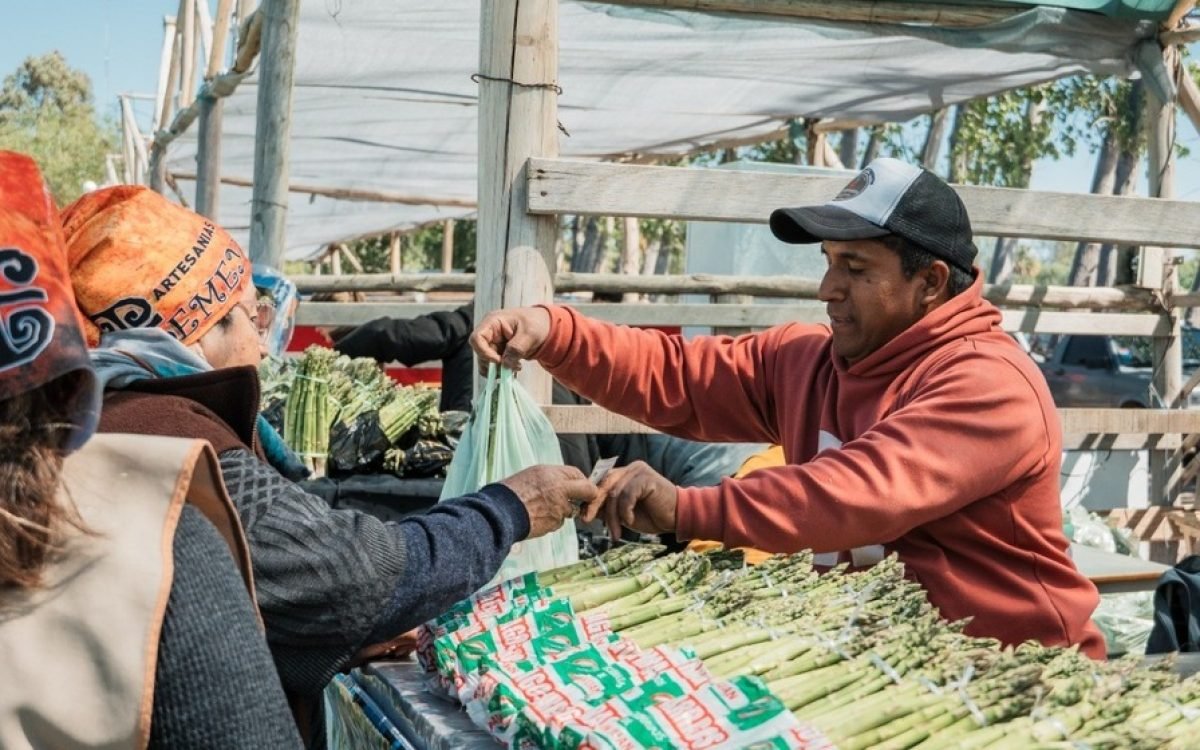 Puesto de espárragos en una feria al aire libre, con un puestero que entrega una bolsa.