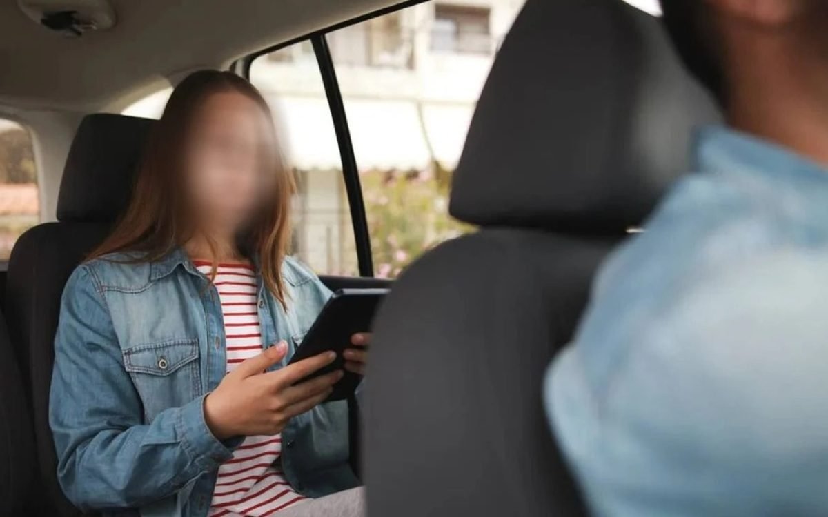 Pasajera en el asiento trasero de un auto con una tableta, detrás del conductor. Imagen ilustrativa.