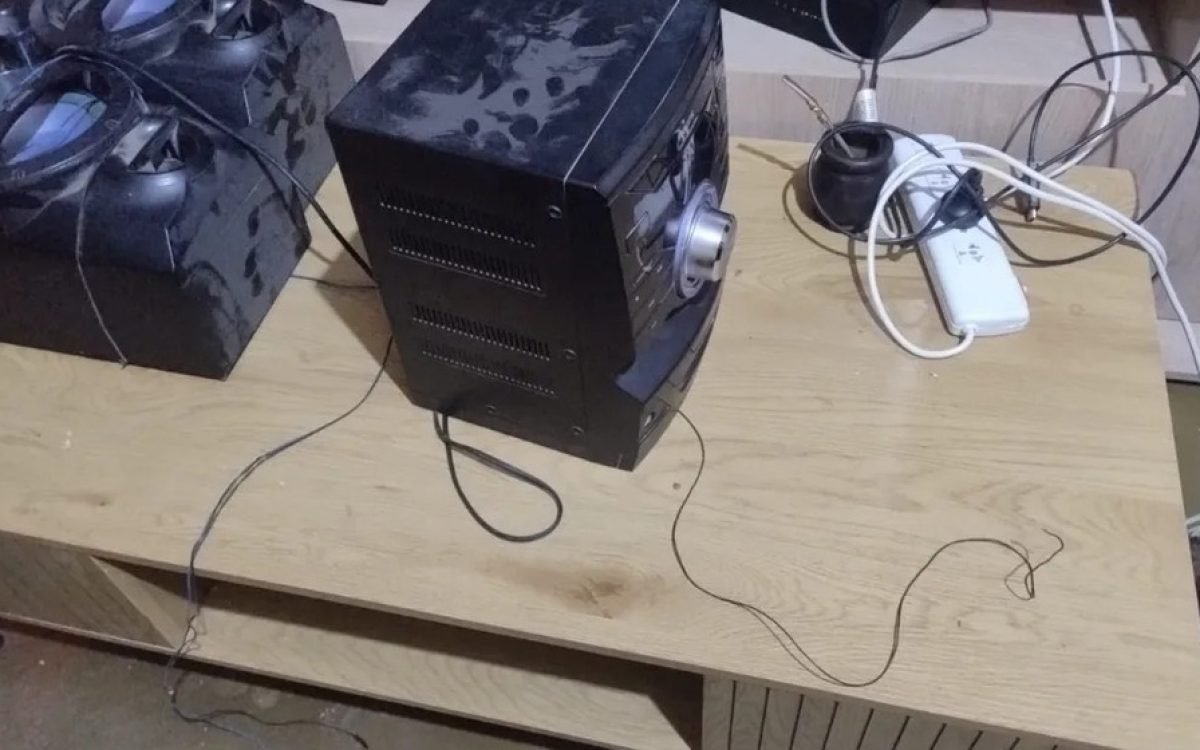 Un centro musical negro con dos parlantes sobre un mueble de madera, con los cables cortados.