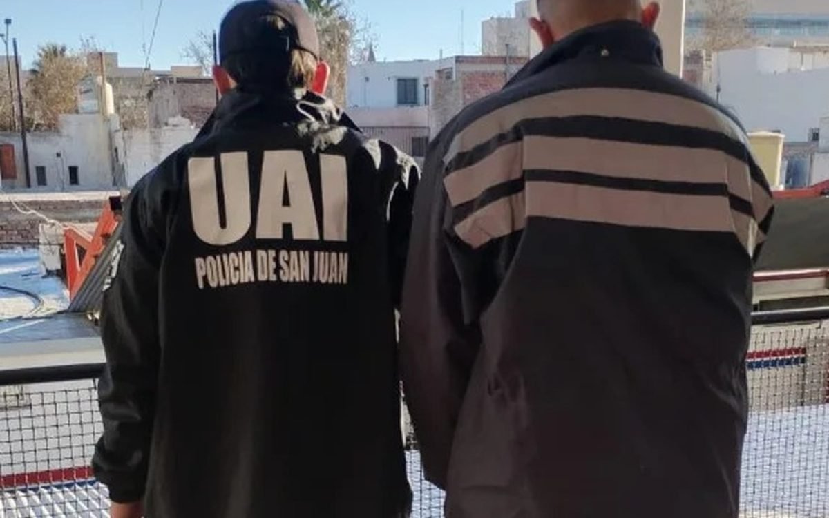 Un efectivo de la UAI de la Policía de San Juan, de espaldas, junto a un detenido.