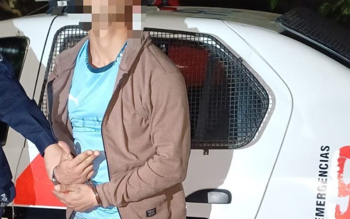 Hombre detenido con la cara pixelada junto a un móvil policial, de noche.