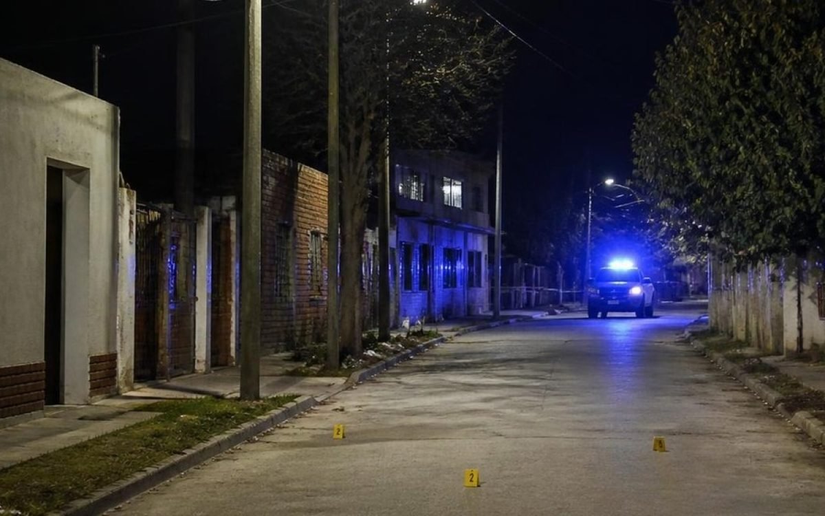 Calle de barrio de noche con un patrullero a lo lejos. Imagen ilustrativa.