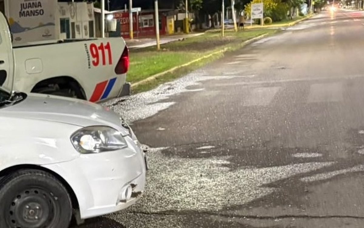 Un Chevrolet Aveo blanco junto a una camioneta policial 911 en una calle de Rawson.