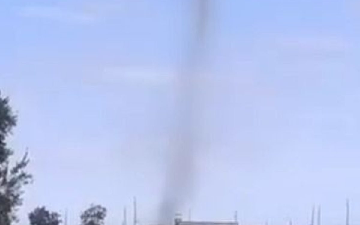 Columna de polvo de un remolino de viento sobre un barrio, con cielo despejado.