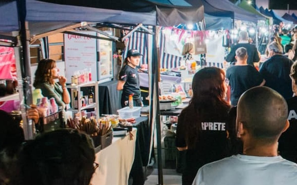 Vecinos recorren de noche los puestos de una feria bajo gazebos azules iluminados en Villa Krause.